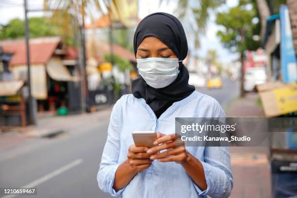 young muslim woman using smartphone on the street - indonesian ethnicity stock pictures, royalty-free photos & images