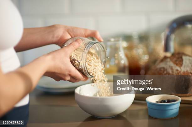 woman pouring oats into bowl in kitchen, close up. - breakfast woman bildbanksfoton och bilder