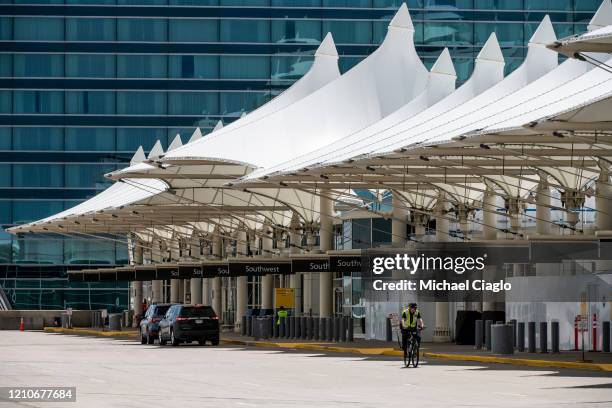 Police officer rides his bike along an empty passenger drop off area at Denver International Airport as the coronavirus pandemic slows air travel on...