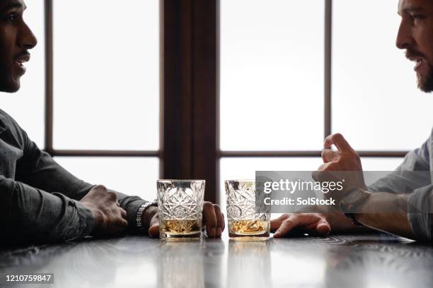 profile view of two men at table with whiskey - whisky bar stock pictures, royalty-free photos & images