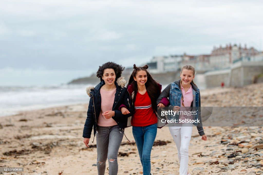 Teenage friends walking arm in arm along windy beach