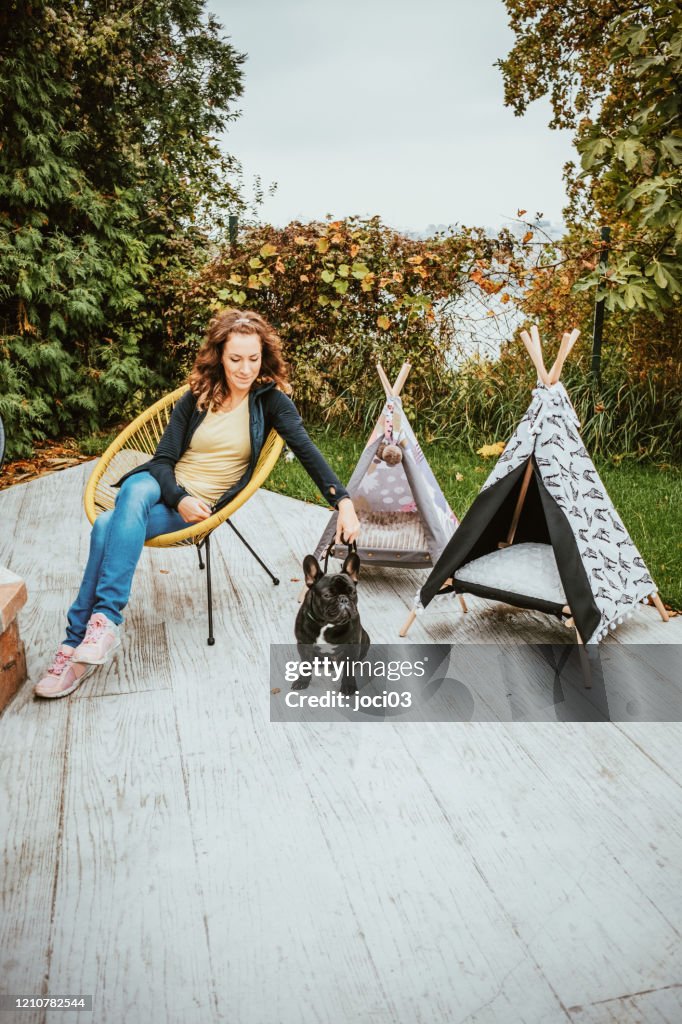 Young woman relaxing with her french bulldog puppy in the garden lounge.