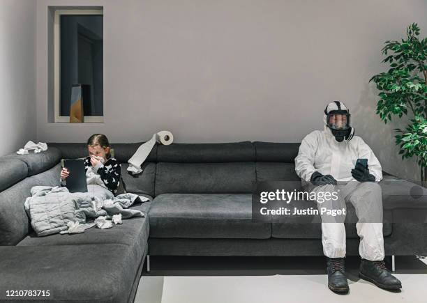 young girls got the flu. dad's in his full protective gear on other end of the sofa! - schutz und arbeitskleidung stock-fotos und bilder