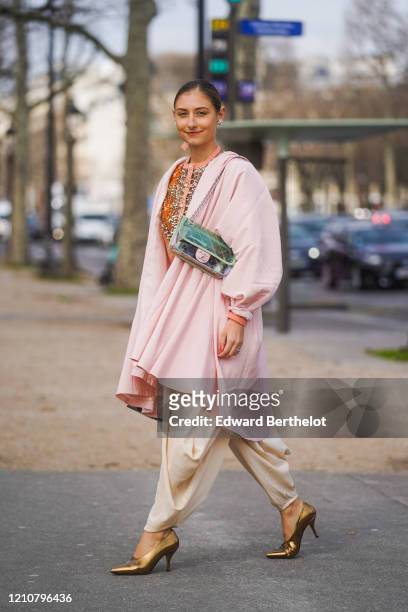 Jenny Walton wears a Chanel bag, a pink long jacket, flowing pants, golden shiny pointy shoes, a bejeweled shirt, earrings, outside Chanel, during...