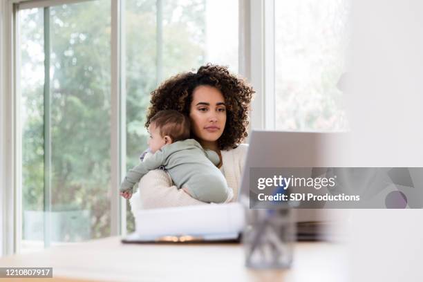 stay-at-home mom holds baby while working remote - stay indoors stock pictures, royalty-free photos & images
