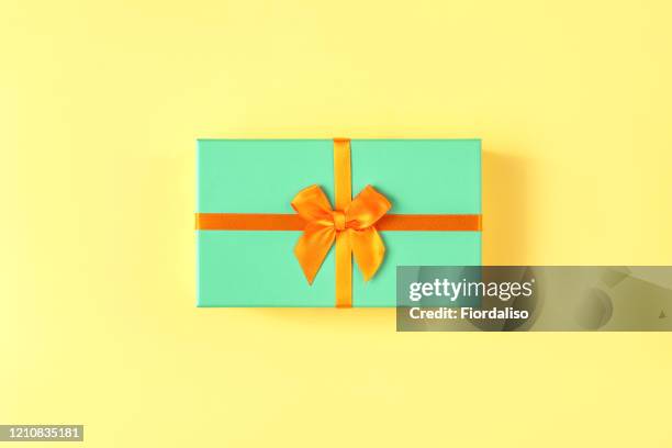 turquoise gift box with orange ribbon tied in a beautiful bow on pastel yellow background - orange silk background stock-fotos und bilder