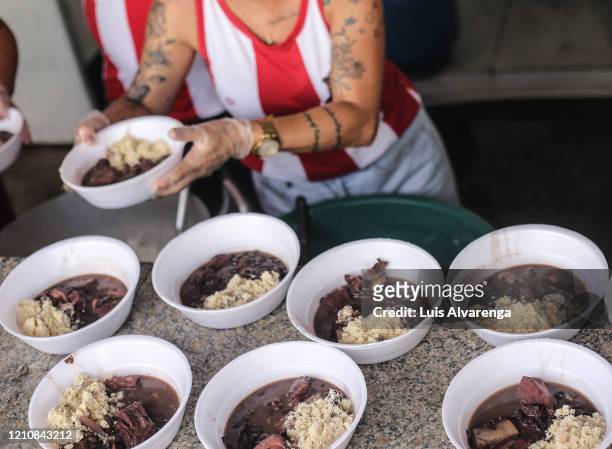 Members of Porto da Pedra Samba School distribute 'feijoada' meals to residents of a community in Sao Goncalo on April 23, 2020 in Niteroi, Brazil....