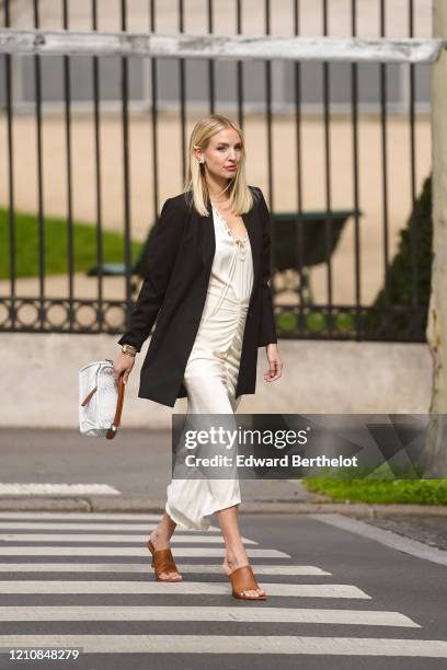 Leonie Hanne wears earrings, a black oversized jacket, a white dress, a white bag, brown pointy shoes, outside Gauchere, during Paris Fashion Week -...