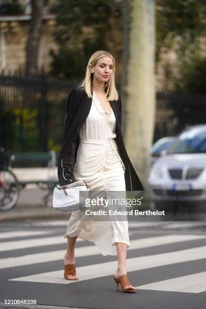 Leonie Hanne wears earrings, a black oversized jacket, a white dress, a white bag, brown pointy shoes, outside Gauchere, during Paris Fashion Week -...