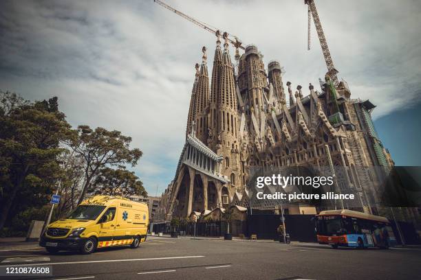 April 2020, Spain, Barcelona: An ambulance drives along an almost deserted road past the "Sagrada Familia" of Gaudi. The town, otherwise flooded with...