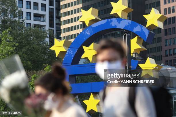 People wearing face masks walk in front of a big Euro sign in Frankfurt am Main, western Germany, as the European Central Bank headquarter can be...
