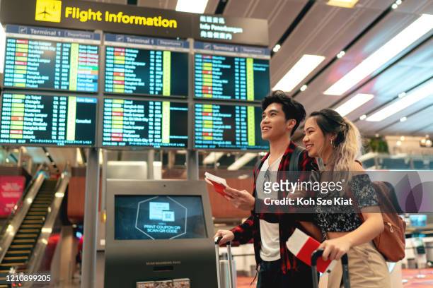 young asian couple at the airport departure board - singapore airport stock pictures, royalty-free photos & images