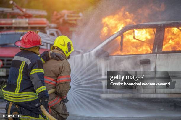 fire fighter hosing water to extinguish a fire over the car in accident on the road - victim services stock pictures, royalty-free photos & images