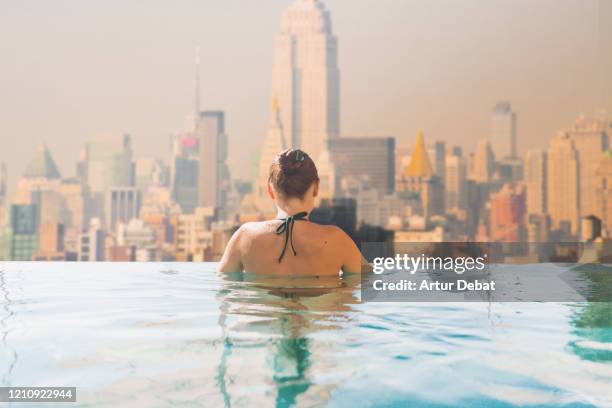 woman in infinity pool rooftop with manhattan skyline view. - rooftop pool stock-fotos und bilder