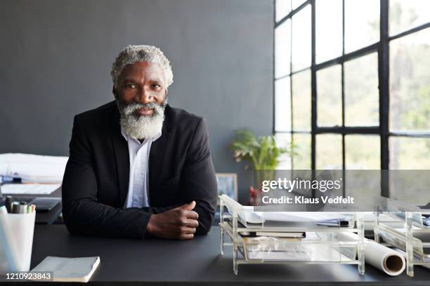 confident businessman sitting at desk in office - black blazer foto e immagini stock