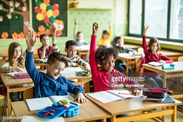 glückliche grundschüler heben ihre hände auf eine klasse in der schule. - kind im grundschulalter stock-fotos und bilder