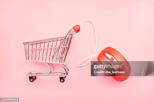 still life of a small shopping cart and red computer mouse on pink background, online shopping - elektronischer handel stock-fotos und bilder