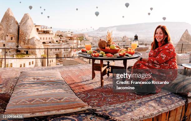 woman dressed in red on a rooftop in cappadocia at sunrise, turkey - cappadocia hot air balloon stock-fotos und bilder