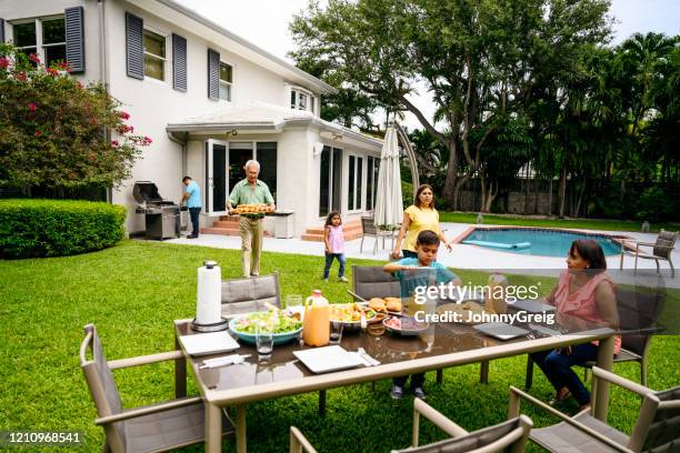 latijns-amerikaanse familiedie bij lijst voor openluchtmaaltijd verzamelt - backyard barbeque stockfoto's en -beelden