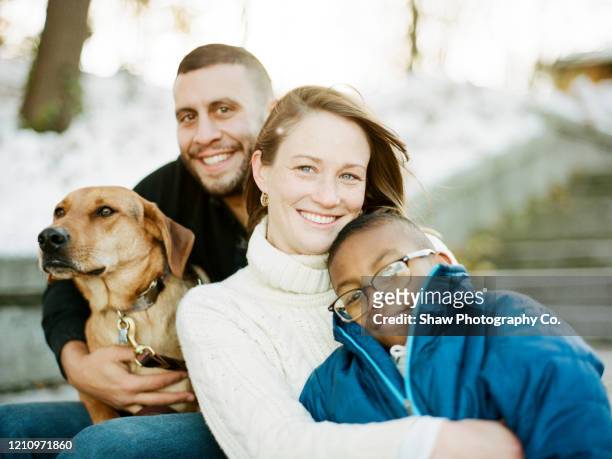 family with adoptive son and adopted dog smiling for a portrait sitting on the steps of stairs in a beautiful park - pet adoption stock-fotos und bilder