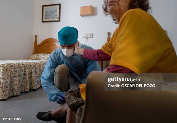 An isolated resident caresses Venezuelan doctor Diego Padron's face as he examines her at an elderly people nursing home in Madrid on April 24, 2020....