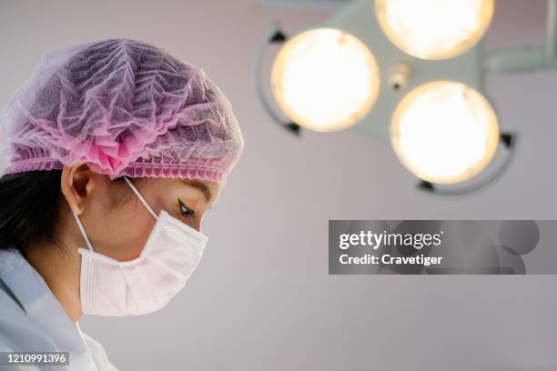 female doctor wearing surgical mask and pink hat while looking down surgeon working in operating room . - oncologist stock pictures, royalty-free photos & images