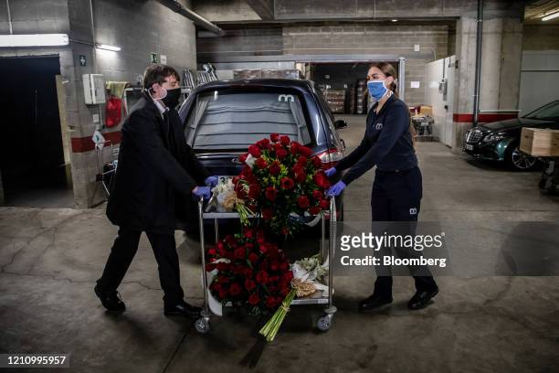 Workers wearing protective face masks wheel a cart containing floral tributes for the deceased into the mortuary at the Memora Servicios Funerarios...