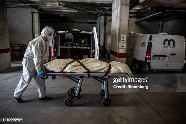 Image depicts death.) A worker dressed in personal protective equipment wheels a trolley containing the body of a victim of coronavirus into the...