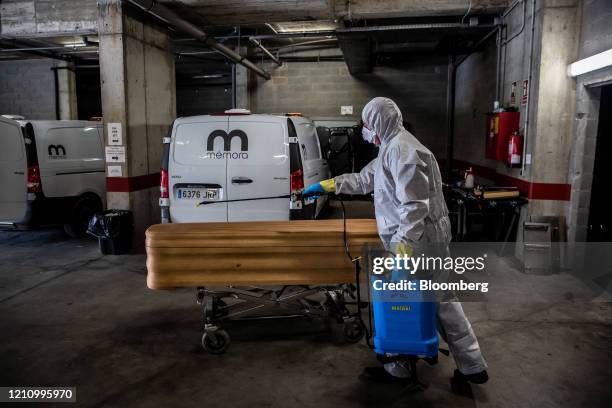 Worker dressed in personal protective equipment sprays disinfectant onto the closed casket containing the body of a victim of coronavirus in the...