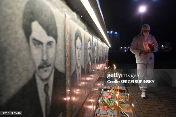 Chernobyl plant employee wearing a face mask lights candles at the monument to Chernobyl victims in Slavutich, the city where the power station's...