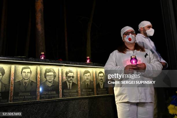 Chernobyl plant workers wearing face masks hold candles at the monument to Chernobyl victims in Slavutich, the city where the power station's...