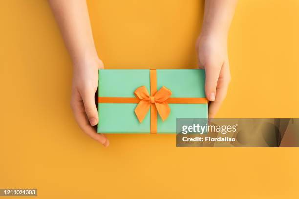 hands of teenage girl holding a green gift box with a yellow satin ribbon on red background - birthday present stockfoto's en -beelden