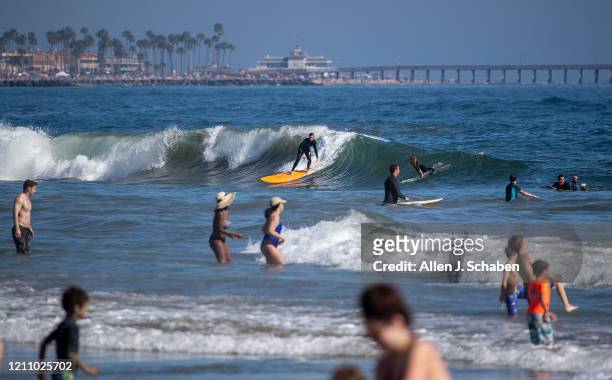 Surfer catches a wave while joining some of the thousands of beach-goers enjoying a warm, sunny day at the beach amid state-mandated stay-at-home and...