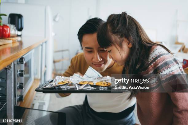 père avec la fille faisant cuire des biscuits ensemble dans la cuisine et sentant des biscuits fraîchement cuits directement du four - odorat photos et images de collection