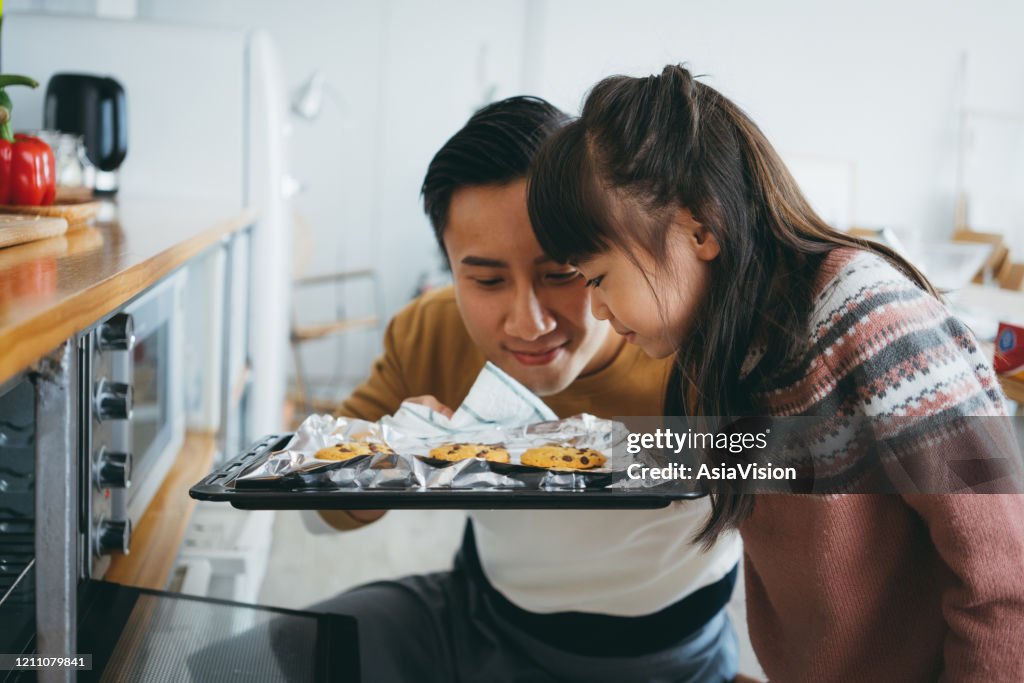 Father with daughter baking cookies together in the kitchen and smelling freshly baked cookies straight from the oven
