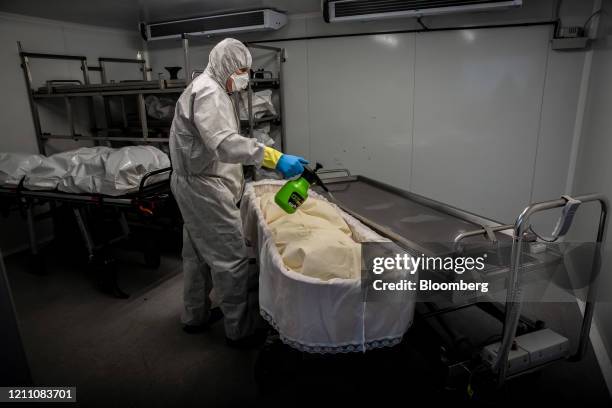 Image depicts death.) A worker dressed in personal protective equipment sprays disinfectant into a casket containing the body of a victim of...