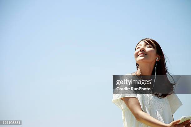 young woman listening to music outside - content japanese ethnicity stock pictures, royalty-free photos & images