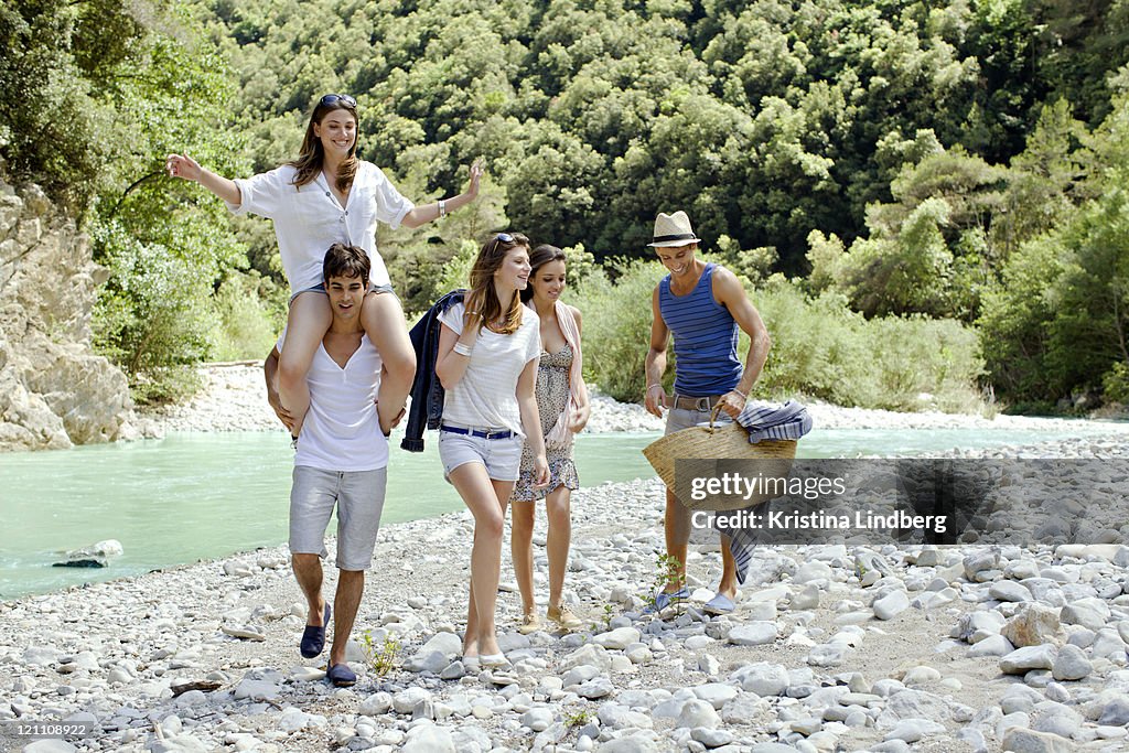 Friends walking, laughing on a riverbank.