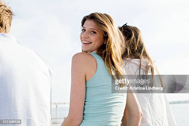 woman with friends by the sea smiling to camera. - regarder par dessus son épaule photos et images de collection
