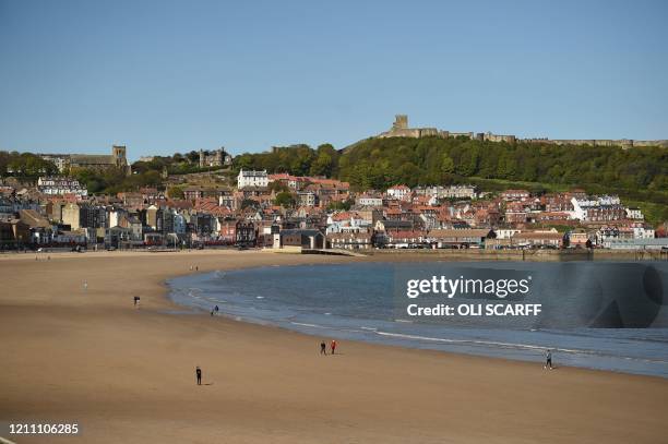 People walk on the beach in Scarborough, northeast England on April 27, 2020 as life continues in Britain under lockdown to help stem the...