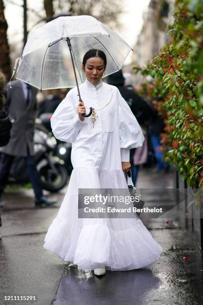 Yoyo Cao wears a white dress/shirt with puff sleeves, a mesh bottom ruffled and pleated part, mandarin collar, a turtleneck wool pullover, a golden...