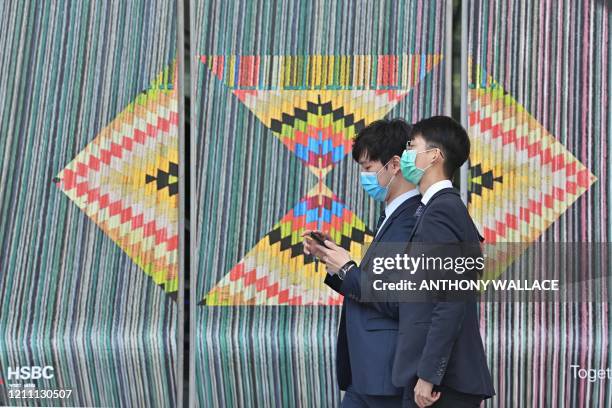 Mask-clad office workers walk past an HSBC logo outside the bank's local headquarters in Hong Kong on April 28, 2020. - The London-based,...