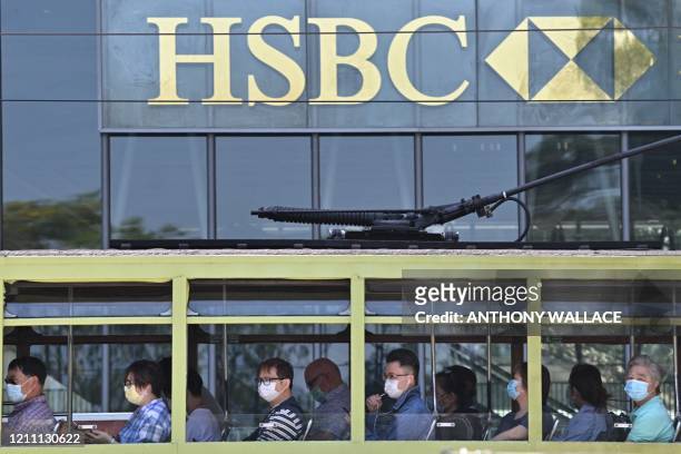 Commuters wearing face masks travel on a tram past HSBC signage displayed outside the bank's local headquarters in Hong Kong on April 28, 2020. - The...