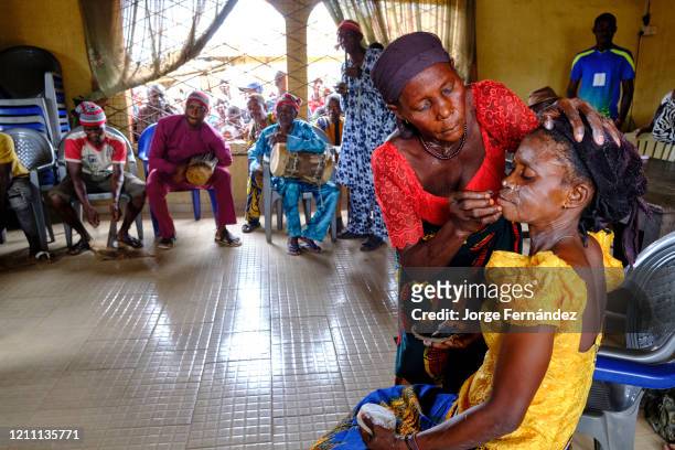 Woman painting the face of another woman with traditional paintings during an Igbo ceremony held in the Elder's Hall.