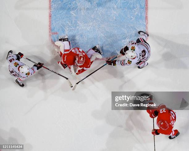 Jonathan Bernier of the Detroit Red Wings makes a save as Alex DeBrincat and Jonathan Toews of the Chicago Blackhawks look for the rebound during an...