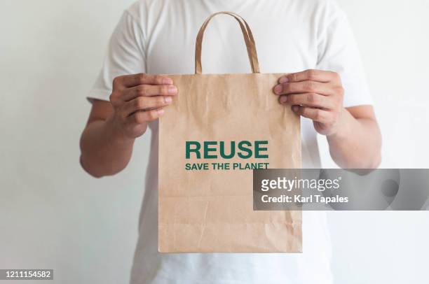 a front view of a young man holding a reusable paper bag on a white background - shopping bag in hand stockfoto's en -beelden
