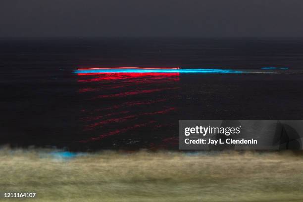 In a long exposure, a boat is seen moving across the water and activating the blue bioluminescence in wave off the coast of Redondo Beach, CA,...