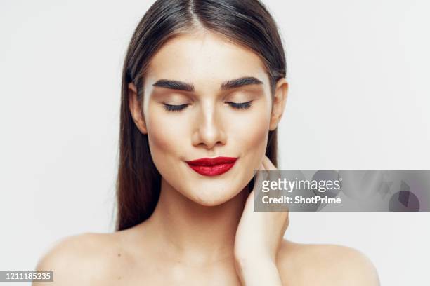 a young woman with an oval face, thick eyebrows and puffy red eyebrows covered her eyes, smiles and gently touches her skin with her hand - thick white women fotografías e imágenes de stock