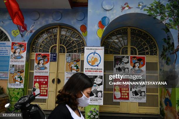 Vietnamese woman, wearing a face mask walks past propaganda posters on preventing the spread of the COVID-19 novel coronavirus, pasted on the gates...