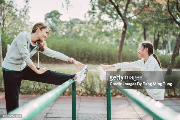 pretty young mom & lovely daughte stretching legs on rail in park joyfully - beautiful asian legs stockfoto's en -beelden